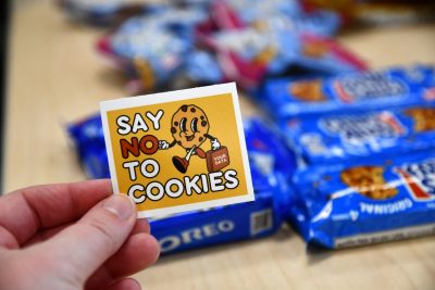 Someone is holding a sticker that says say no to cookies with a cookie cartoon character holding a briefcase labeled your data.