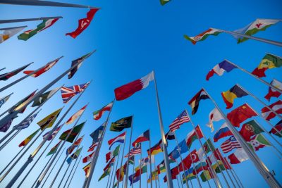 Dozens of colorful international flags against a bright blue sky.